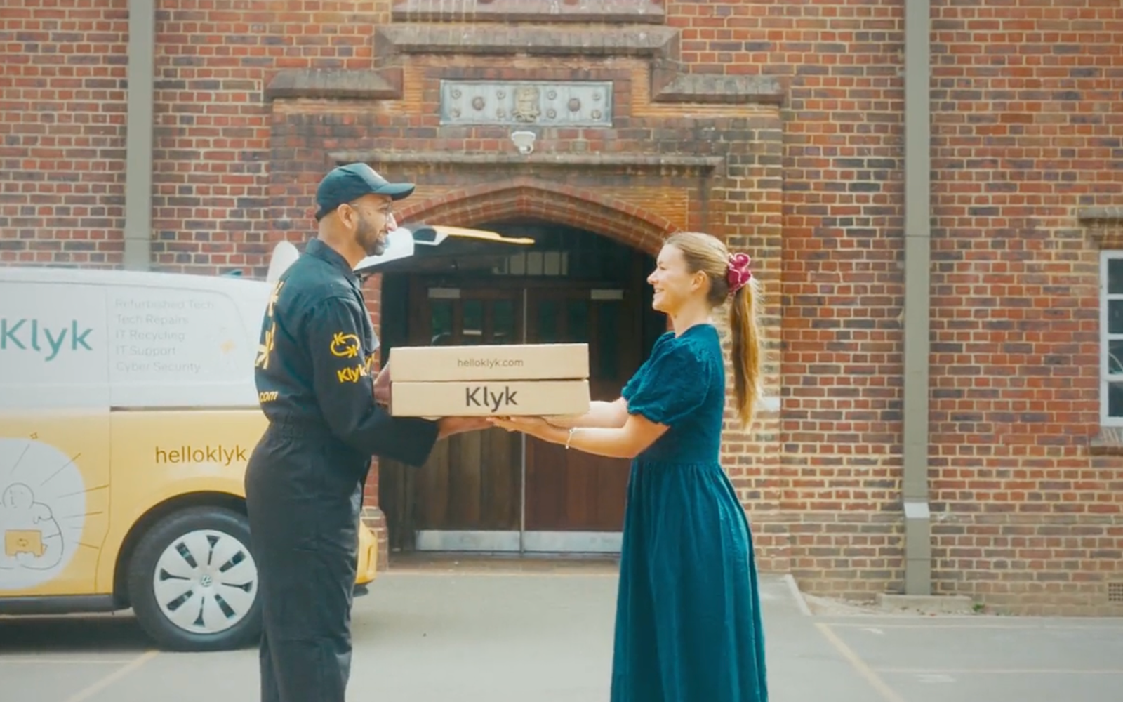 A Klyk engineer handing boxed laptops to a teacher outside a school