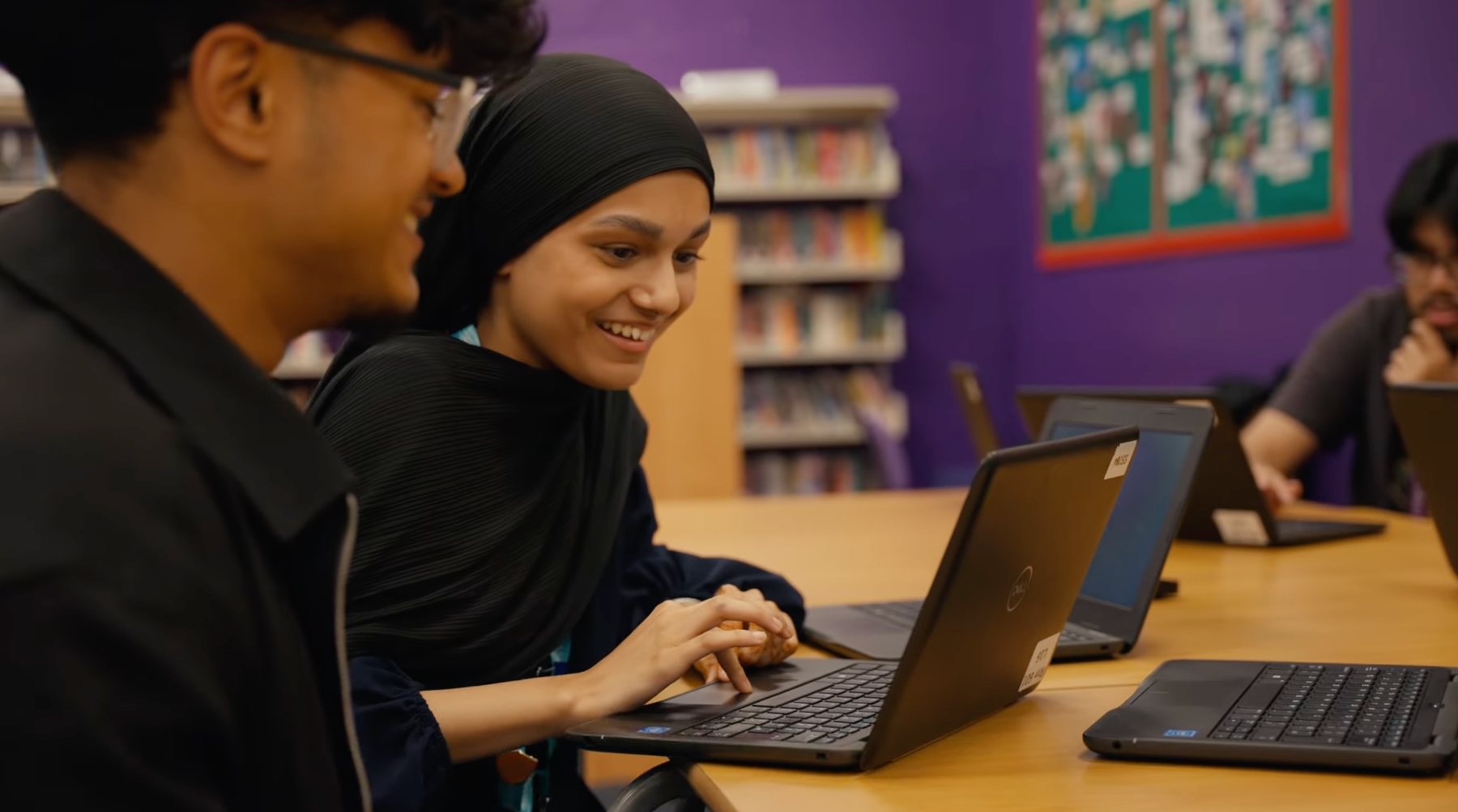 Students smiling as they use donated laptops in a school library